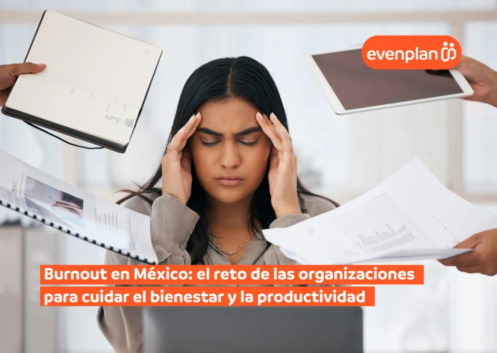 Mujer con las manos en la cabeza rodeada de papeles, cuadernos y una tablet, transmitiendo estrés por carga de trabajo y burnout.