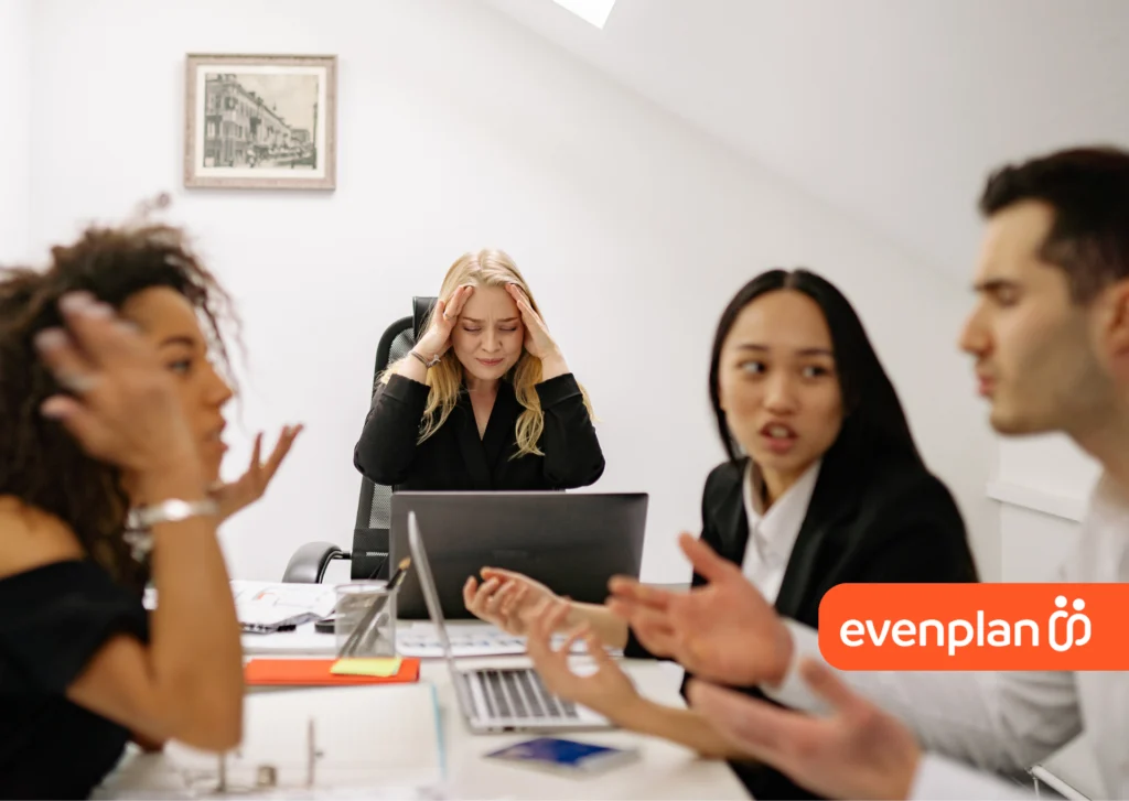 Team meeting around a table; a frustrated blonde woman head in hands at center, looking at a laptop while colleagues discuss. Evenplan logo in the bottom-right.